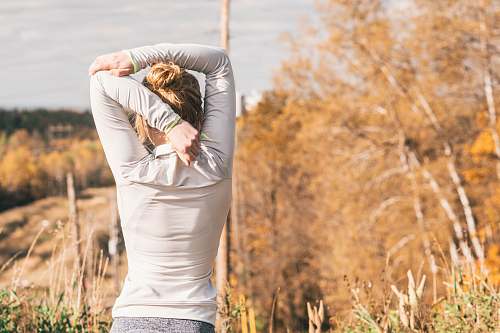 human woman standing while stretching beside brown leafed trees people