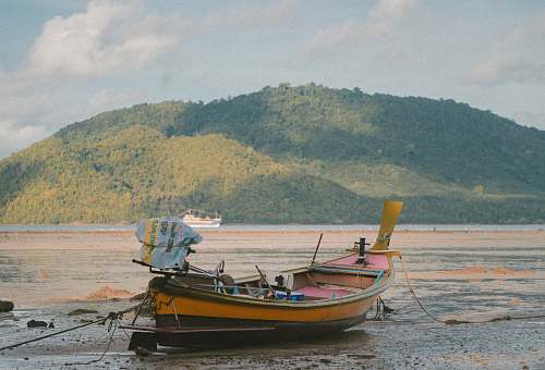 transportation orange boat on seashore during daytime across mountain vessel