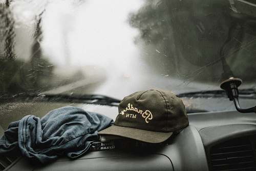 cap black and white baseball cap near grey shirt on top of glove compartment inside car trip