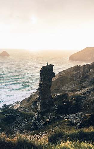 cliff man standing on rock cliff near body of water sea