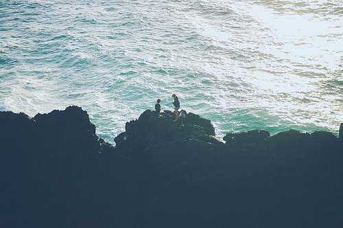 sea two person standing on the cliff near the ocean rocks