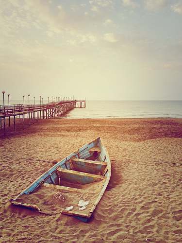 boat blue canoe boat on brown sand near brown wooden dock and body of water during daytime sand