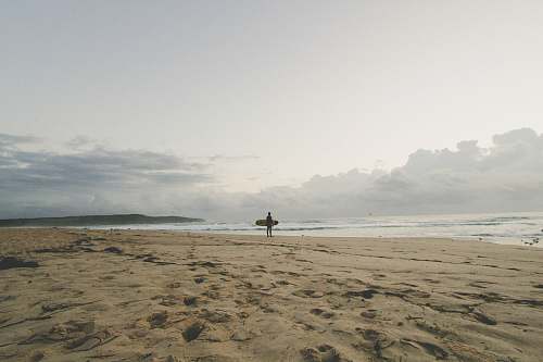 surfer man standing by the seashore with surfboard sand