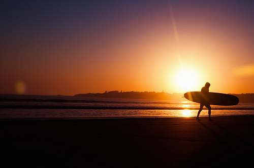 ocean silhouette of man holding surfboard near seashore during sunset surf