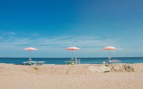 ocean three empty beach loungers with umbrellas overlooking the beach under blue sky coast