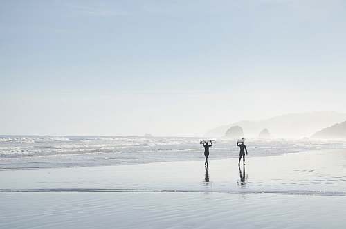grey two men carrying surfboards near body of water coast