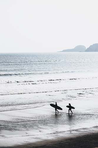 ocean two people carrying surfboards at beach during daytime grey
