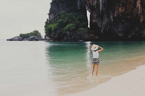 sand woman on body of water beside mountain ocean