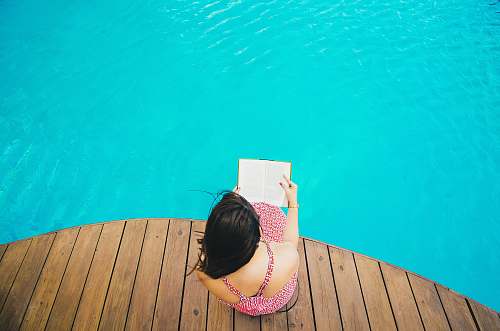 blue woman sitting on poolside dock while riding book woman