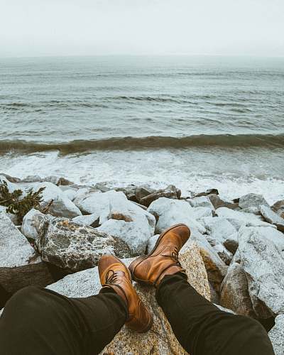 boots person sitting front of seashore waves