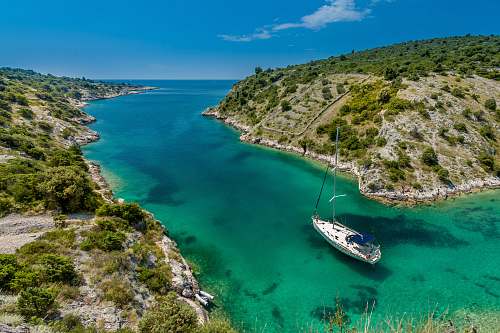 blue aerial photography of white boat near body of water between green mountain during daytime yacht