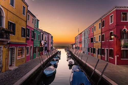 building blue boats parked on river between multicolored buildings at sunset city