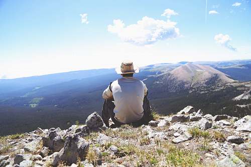 mountain person sitting on a gray rock watching over a mountain mountains