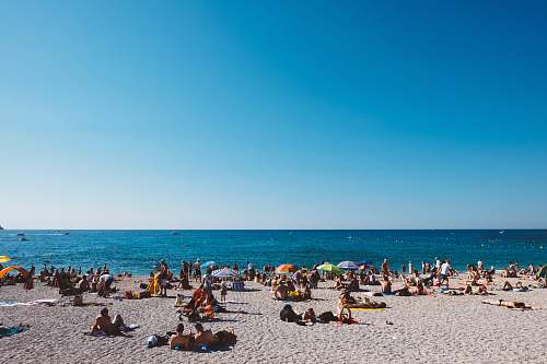 beach group of people enjoying the gray sanded beach with calm water during daytime coast
