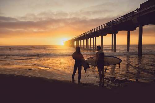 sea woman carrying surfboard beside person during sunset surfboard