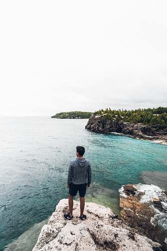 person man standing on white and brown rock seeing horizon during daytime water