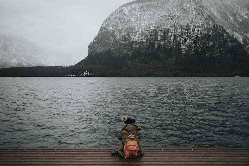 person person sitting on wooden dock in front of body of water hallstatt