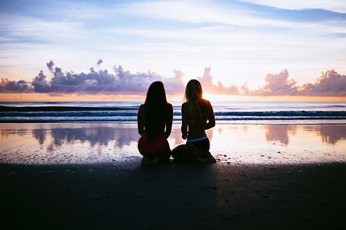 human silhouette of two women facing body of water beach