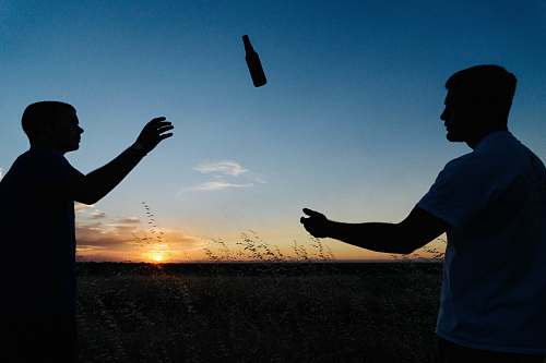 person silhouette photo of two men throwing bottle during daytime silhouette