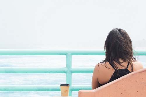 person woman sitting on chair beside cup in front of body of water water