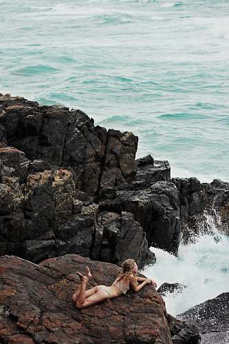 water woman lying on rock formation on seashore bikini