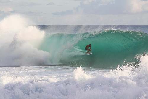 surfing man riding surfboard under sea wave during daytime ocean