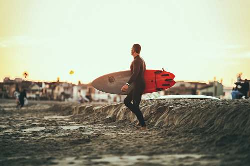 human person carrying surfboard on mud during daytime sand