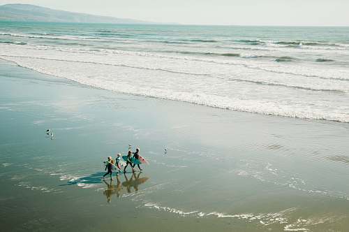 surfing people carrying surfboards walking along seashore beach