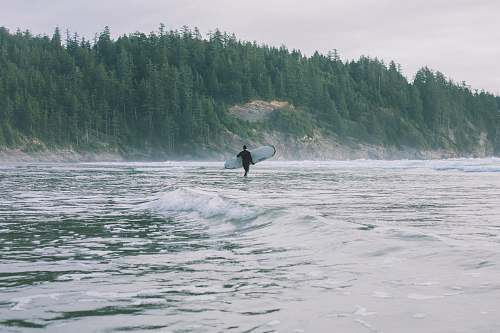 surfboard person walking on shore while holding surfboard during daytime grey