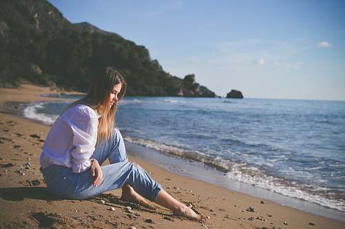 beach woman sitting on beach shore during daytime woman