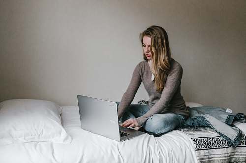 computer woman typing on MacBook Pro while sitting on bed in room laptop