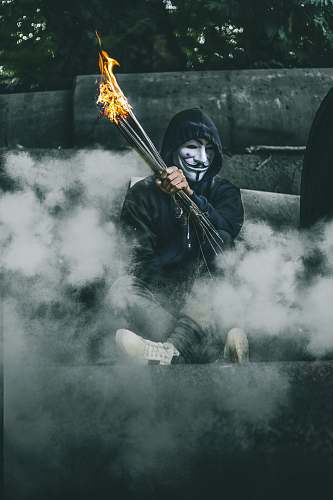 grey person wearing guy Fawkes's mask while holding torch hoodie