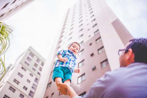 smile shallow focus photography of father holding his son in right hand building