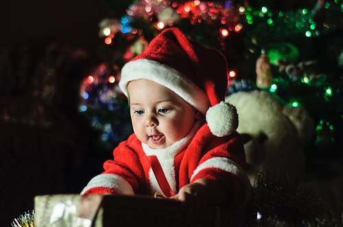 people baby wearing Santa Claus outfit near Christmas tree person