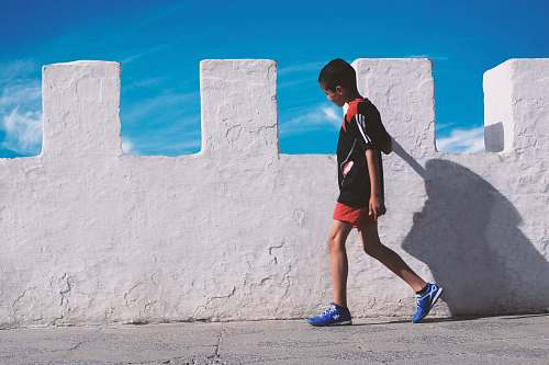 person boy walking beside white concrete wall people