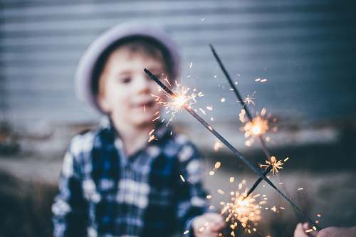 person closeup photo of boy wearing blue and white plaid sport shirt holding firework kid