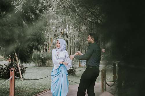 person man smiling looking at woman smiling and standing on bridge near green leaf trees during daytime people