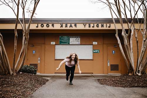person woman laughing and running in front of Lindley Park Pool building during day people