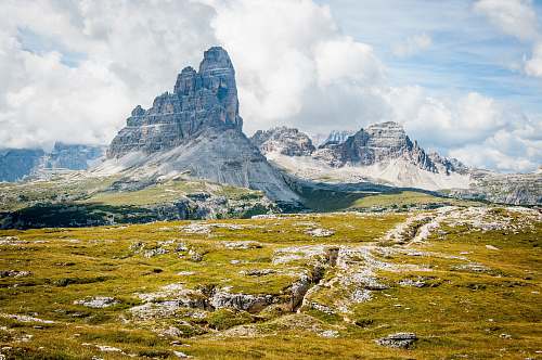 mountain rock formation on wide field grass under cloudy blue sky during daytime landscape