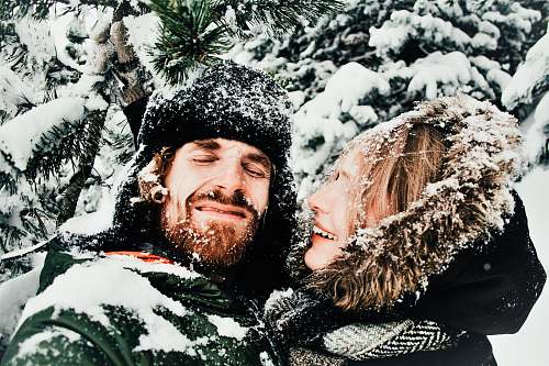 snow smiling man and woman standing under snow covered tree winter