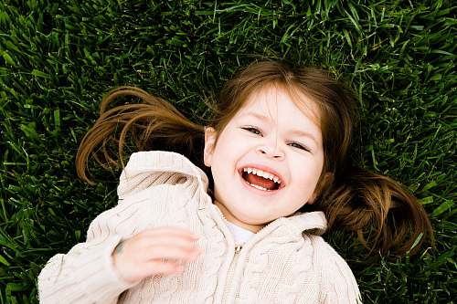 human girl smiling while lying on grass field at daytime person