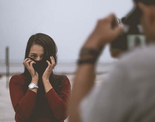 human selective focus photography of person wearing white shirt taking photo of woman wearing red long-sleeved shirt covering her face with hair person