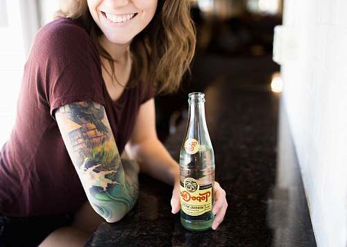 people candid photography of woman holding bottle with broad smile tattoo