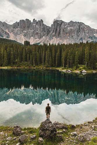 human person standing on cliff in front of forest water