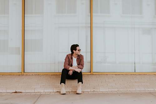 people photo of man sitting on brown bricks against glass wall human