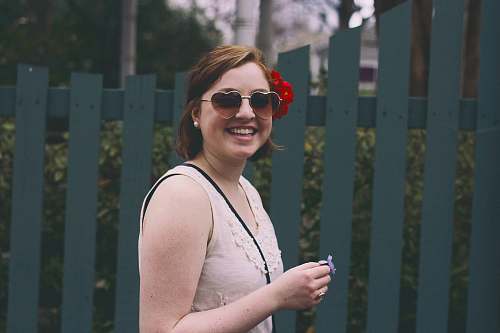 people woman standing while smiling beside blue wooden fence human