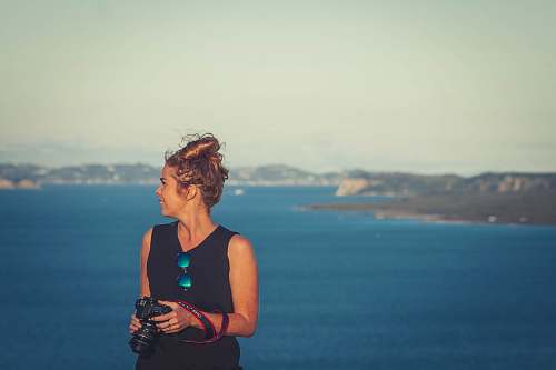 woman woman wearing black V-neck sleeveless dress holding DSLR camera in front of sea female