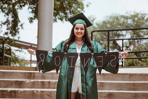 girl woman wearing green academic dress holding black seniors-printed buntings graduation