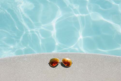 summer gold framed orange lens Aviator-style sunglasses beside pool glasses
