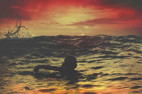 sunset person swimming on body of water under red and orange sky sunrise